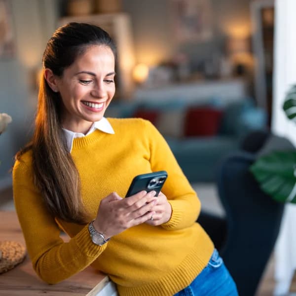 A woman in a yellow sweater smiles while using her phone, likely engaging with interac e-transfer services.