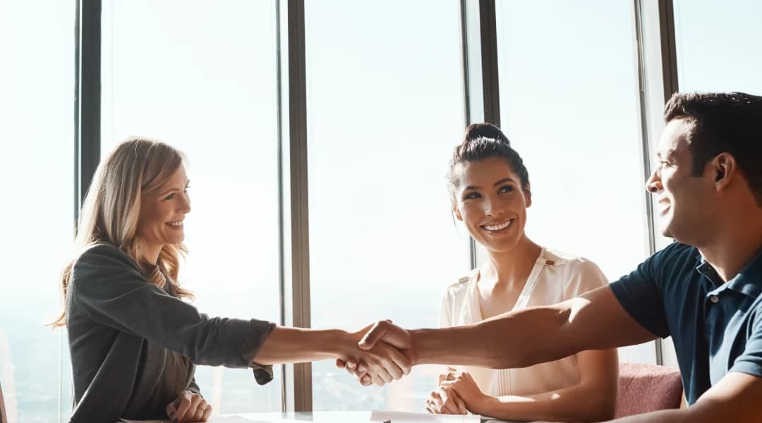 Three business professionals shaking hands in an office, symbolizing partnership and collaboration in the Loans 24/7 sector.