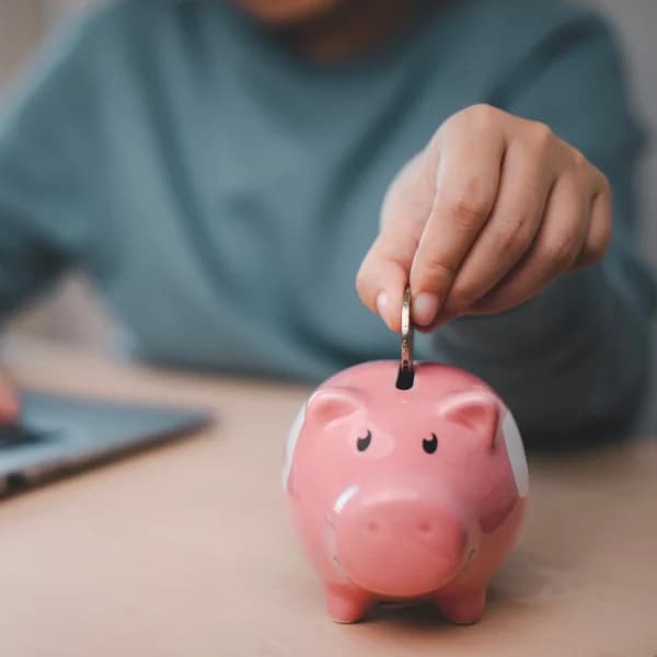 A person inserting money into a piggy bank, symbolizing savings and the management of personal finances.
